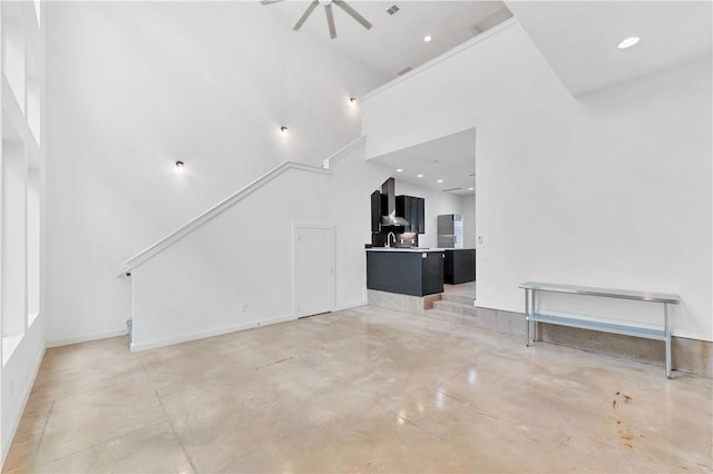 unfurnished living room featuring ceiling fan and a towering ceiling