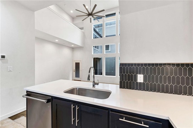 kitchen featuring a towering ceiling, tasteful backsplash, ceiling fan, sink, and dishwasher