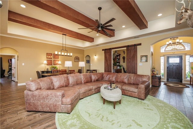 living room with beam ceiling, a barn door, hardwood / wood-style flooring, ceiling fan with notable chandelier, and ornamental molding