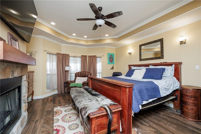 bedroom with ceiling fan, a stone fireplace, crown molding, and dark wood-type flooring