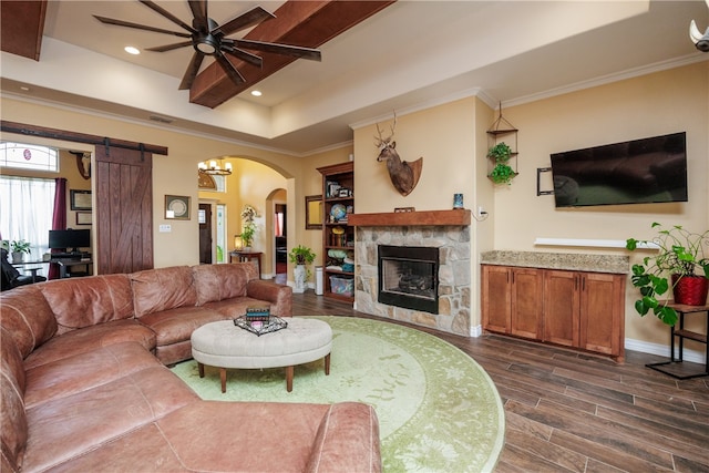 living room featuring a barn door, crown molding, dark wood-type flooring, and ceiling fan with notable chandelier