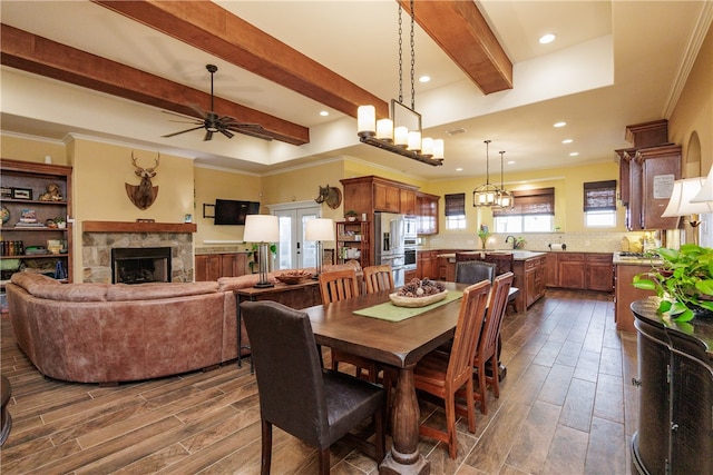 dining area with a stone fireplace, crown molding, dark hardwood / wood-style flooring, and ceiling fan with notable chandelier