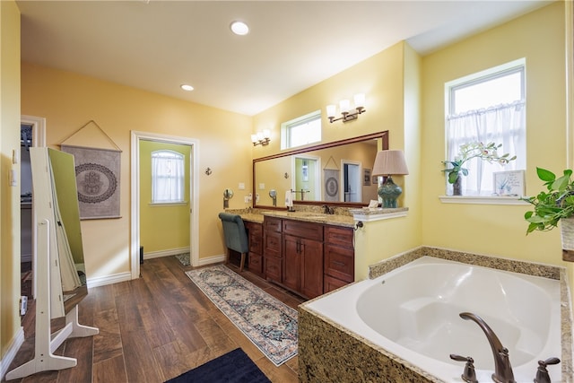 bathroom featuring hardwood / wood-style floors, vanity, a wealth of natural light, and tiled tub