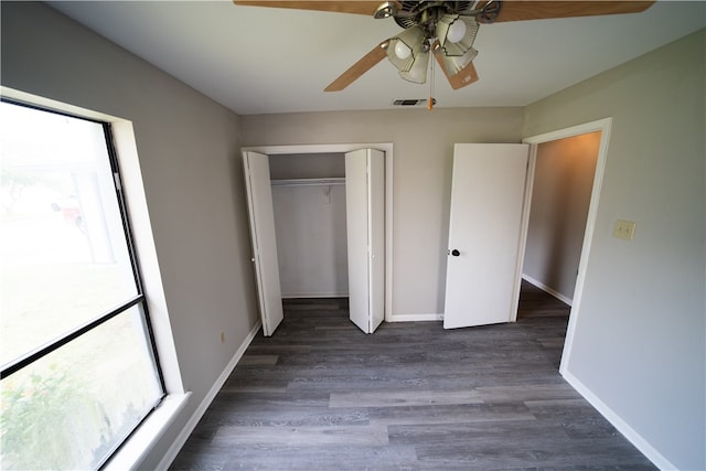 unfurnished bedroom with dark wood-type flooring, a closet, multiple windows, and ceiling fan