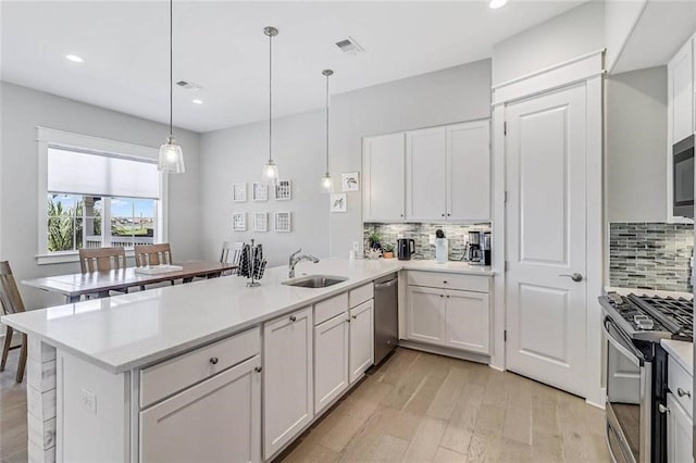 kitchen with sink, hanging light fixtures, appliances with stainless steel finishes, kitchen peninsula, and white cabinets