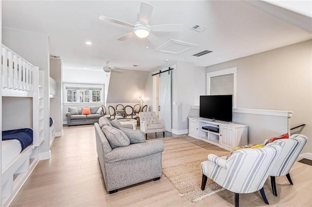 living room with ceiling fan, a barn door, and light wood-type flooring