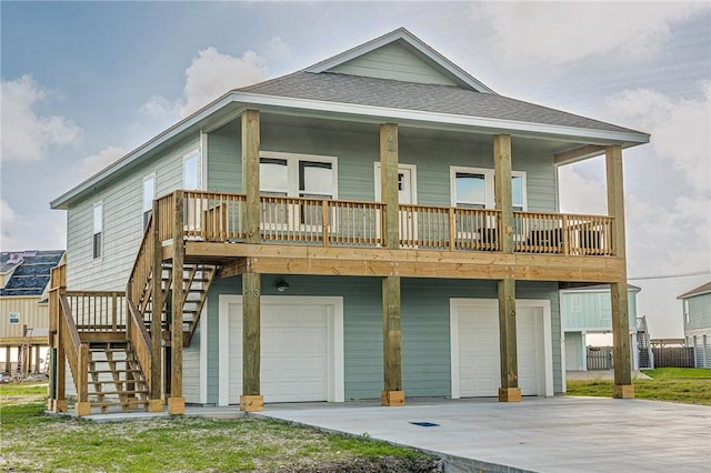 rear view of house featuring roof with shingles, covered porch, concrete driveway, an attached garage, and stairs