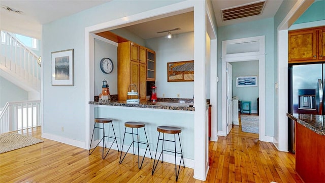 kitchen featuring a breakfast bar area, stainless steel fridge, dark stone counters, kitchen peninsula, and light hardwood / wood-style flooring