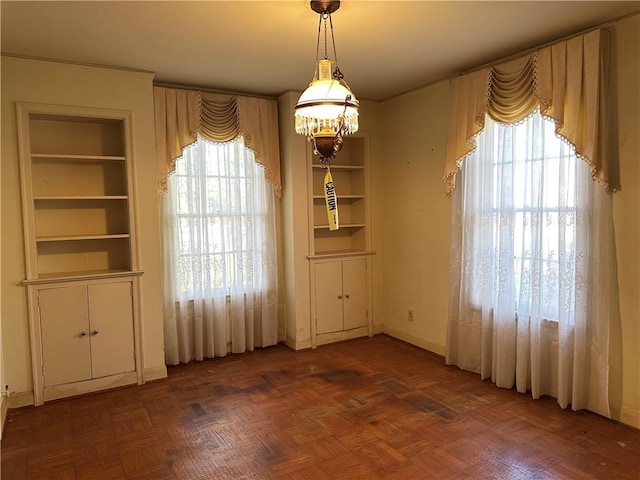 unfurnished dining area featuring dark parquet flooring, built in features, and a wealth of natural light