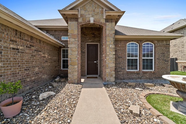 view of exterior entry with roof with shingles and brick siding
