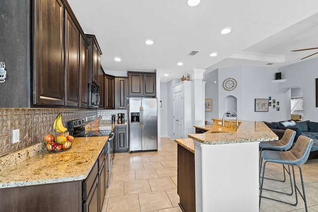kitchen with dark brown cabinets, appliances with stainless steel finishes, a kitchen breakfast bar, open floor plan, and backsplash