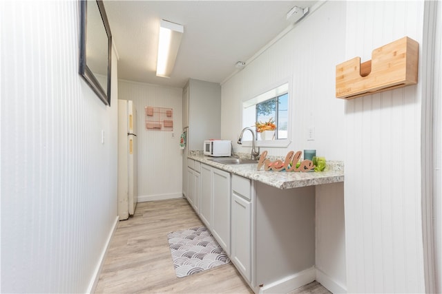 kitchen featuring light wood-type flooring, light stone countertops, wooden walls, sink, and white appliances