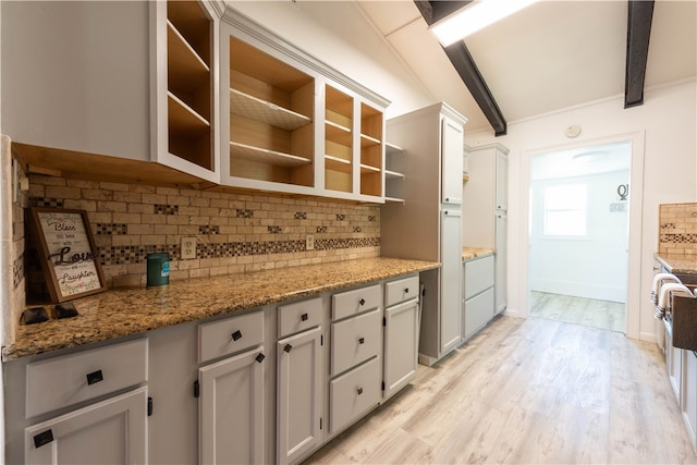 kitchen with beamed ceiling, light stone counters, backsplash, and light hardwood / wood-style flooring