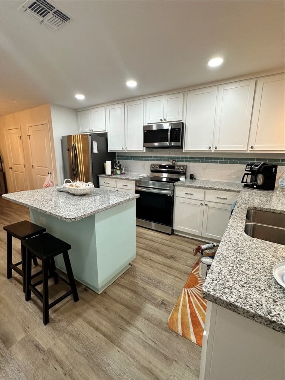 kitchen with light hardwood / wood-style floors, white cabinetry, appliances with stainless steel finishes, light stone countertops, and a center island