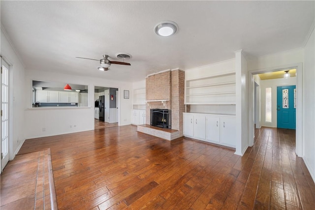 unfurnished living room featuring ceiling fan, built in features, a brick fireplace, and hardwood / wood-style floors