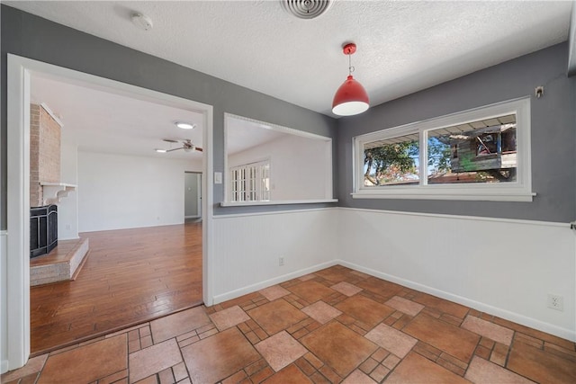 unfurnished dining area with a textured ceiling, ceiling fan, and a large fireplace