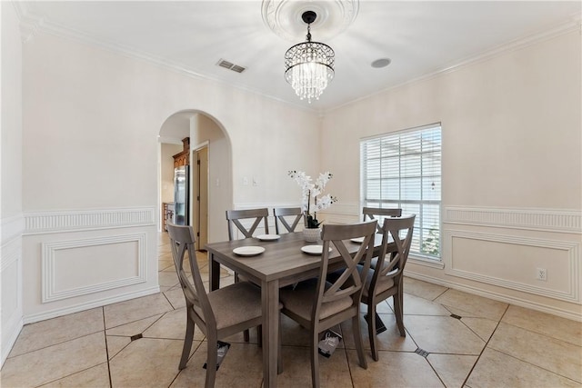 6530 Picante Dr, Corpus Christi, TX 78414 - dining room featuring light tile patterned floors, arched walkways, a chandelier, crown molding, and a wainscoted wall