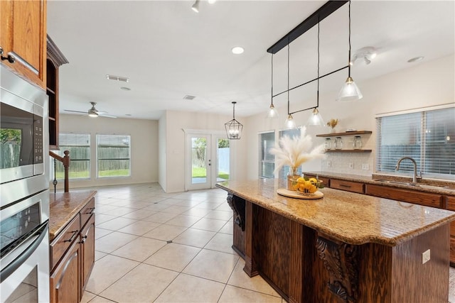 6530 Picante Dr, Corpus Christi, TX 78414 - kitchen featuring stainless steel appliances, a kitchen island, light tile patterned floors, brown cabinetry, and pendant lighting