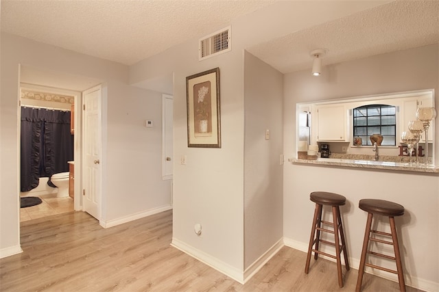 4445 Cedar Pass Dr Unit 103, Corpus Christi, TX 78413 - kitchen with a textured ceiling, light wood finished floors, white cabinets, a breakfast bar, and light countertops