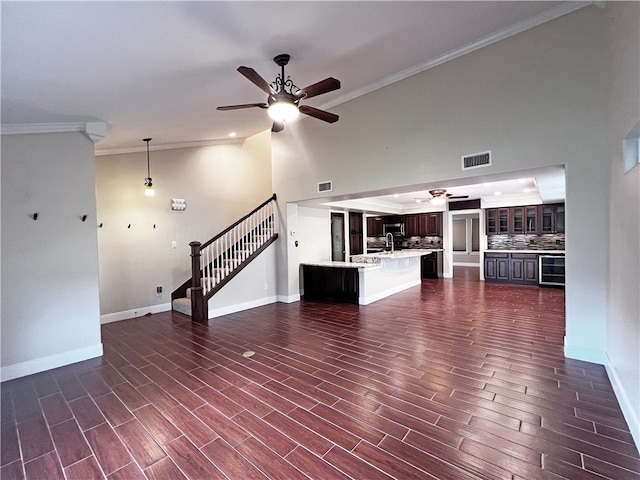 unfurnished living room featuring a high ceiling, wine cooler, crown molding, and dark wood-type flooring