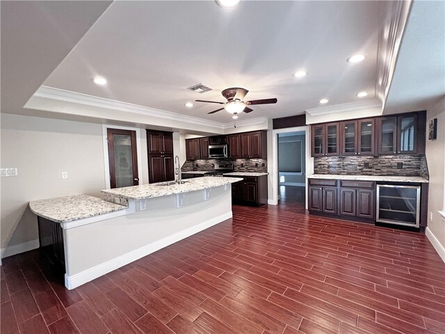 kitchen featuring appliances with stainless steel finishes, dark hardwood / wood-style flooring, tasteful backsplash, dark brown cabinets, and a kitchen island with sink