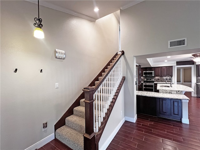 stairs featuring a raised ceiling, wood-type flooring, sink, and ornamental molding