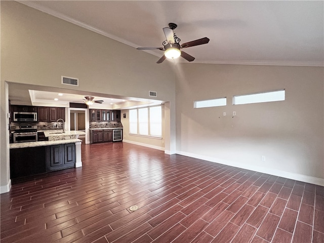 unfurnished living room featuring dark wood-type flooring, a high ceiling, sink, ceiling fan, and ornamental molding