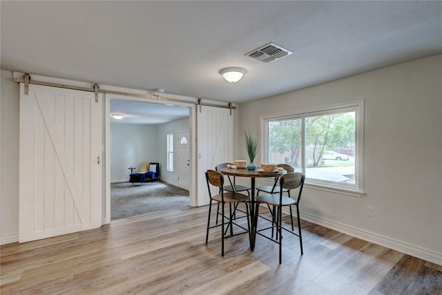 dining space with light wood-type flooring, a barn door, and a textured ceiling