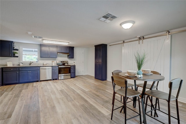 kitchen with stainless steel appliances, a barn door, sink, and light hardwood / wood-style flooring