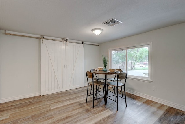 dining area with light wood-type flooring, a barn door, and a textured ceiling