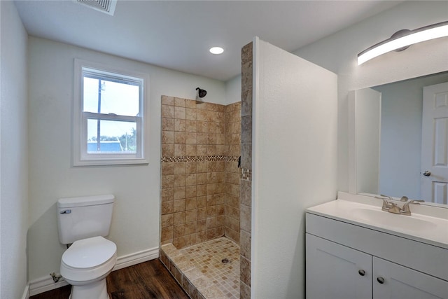 bathroom with wood-type flooring, vanity, toilet, and a tile shower