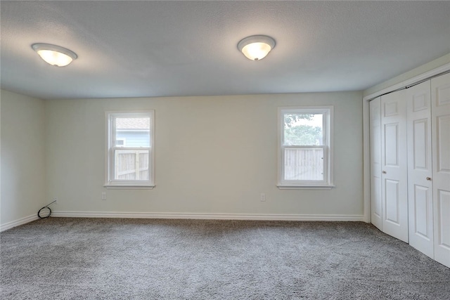 unfurnished bedroom with a closet, multiple windows, a textured ceiling, and carpet flooring