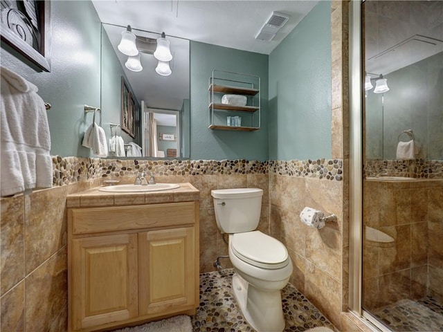 bathroom featuring tile patterned flooring, toilet, vanity, a shower with shower door, and tile walls