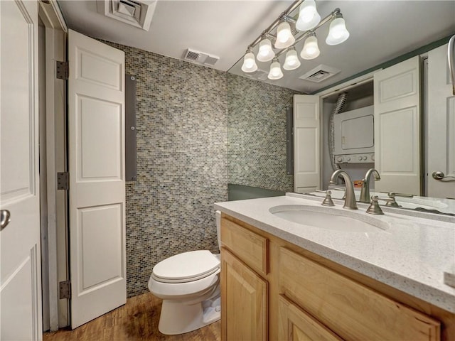 bathroom featuring vanity, hardwood / wood-style flooring, a notable chandelier, toilet, and stacked washer / drying machine