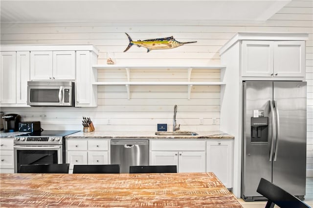 kitchen with light stone countertops, appliances with stainless steel finishes, wooden walls, white cabinets, and sink