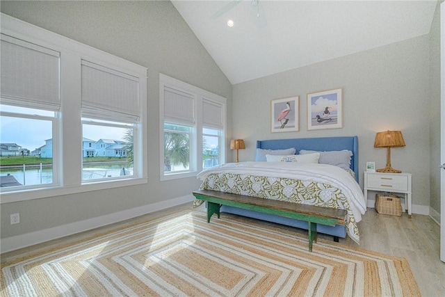 bedroom with light wood-style floors, multiple windows, high vaulted ceiling, and baseboards