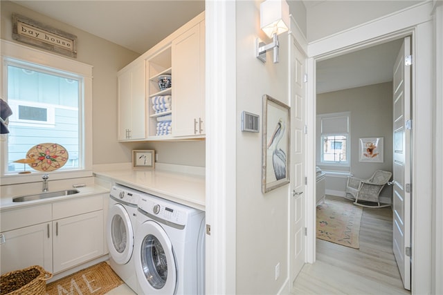 clothes washing area with light wood-type flooring, washer and dryer, cabinet space, and a sink