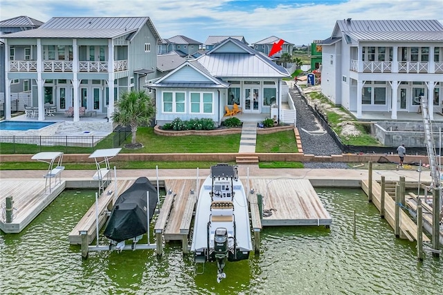 rear view of house with boat lift, a water view, a standing seam roof, metal roof, and a residential view