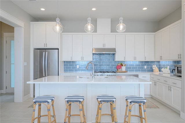 kitchen featuring under cabinet range hood, a center island with sink, white cabinetry, and light countertops