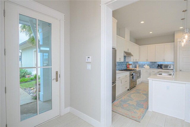 kitchen featuring light countertops, appliances with stainless steel finishes, hanging light fixtures, and white cabinets