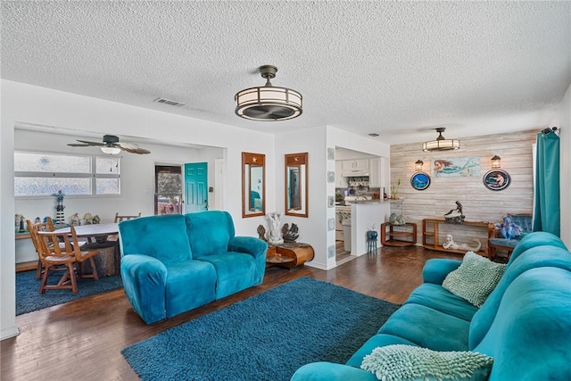 living room with wood finished floors, visible vents, wood walls, and a textured ceiling