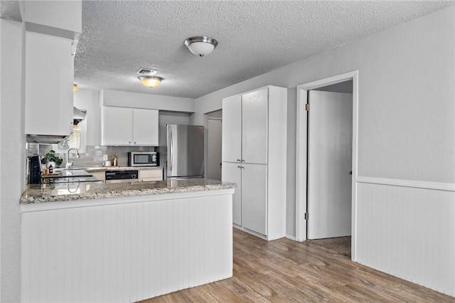 kitchen featuring kitchen peninsula, a textured ceiling, stainless steel appliances, white cabinetry, and range hood