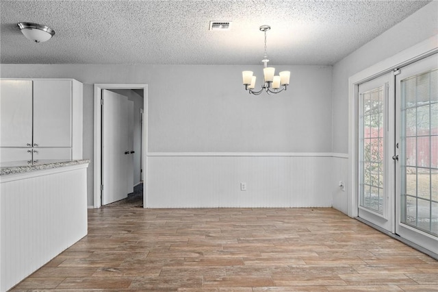 unfurnished dining area with a chandelier, a textured ceiling, and light hardwood / wood-style floors