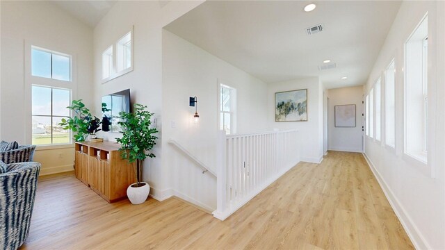 hall with light wood-style flooring, a healthy amount of sunlight, baseboards, and visible vents