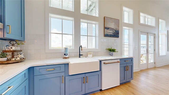 kitchen with tasteful backsplash, blue cabinets, a sink, white dishwasher, and light wood finished floors