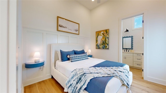 bedroom with a decorative wall, light wood finished floors, and ensuite bath