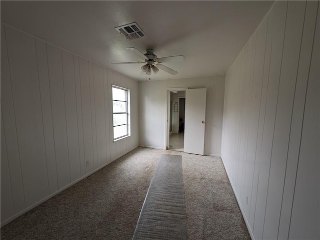 spare room featuring ceiling fan, light carpet, and wooden walls