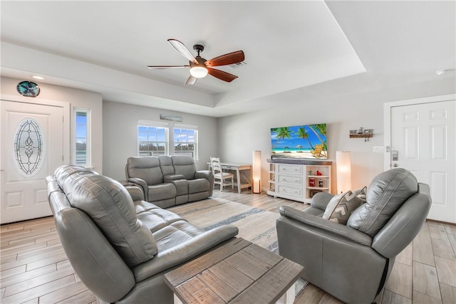 living room featuring light hardwood / wood-style flooring, a raised ceiling, and ceiling fan