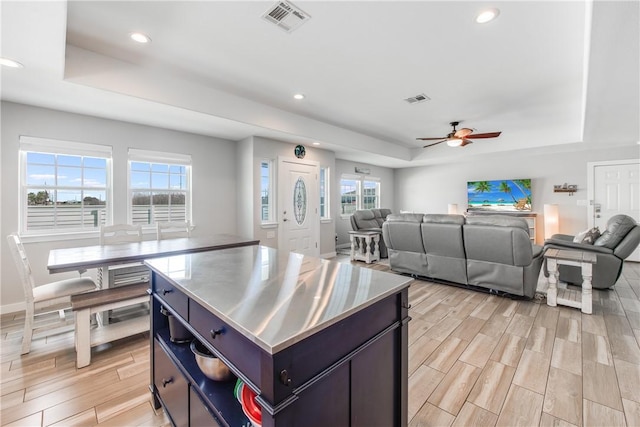 kitchen with ceiling fan, a kitchen island, a raised ceiling, and stainless steel counters