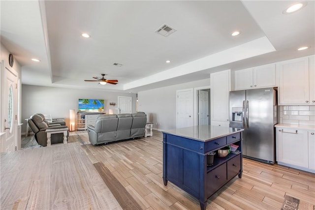 kitchen featuring stainless steel fridge with ice dispenser, a raised ceiling, white cabinets, and a kitchen island